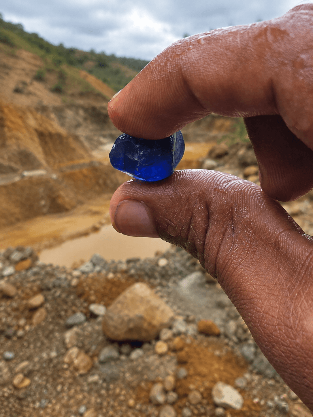 Rough blue sapphire held above an active Sri Lankan gem mine